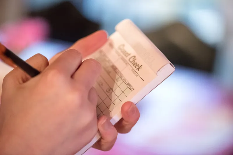 Close-up of hands holding a printed guest list with a laptop in the background