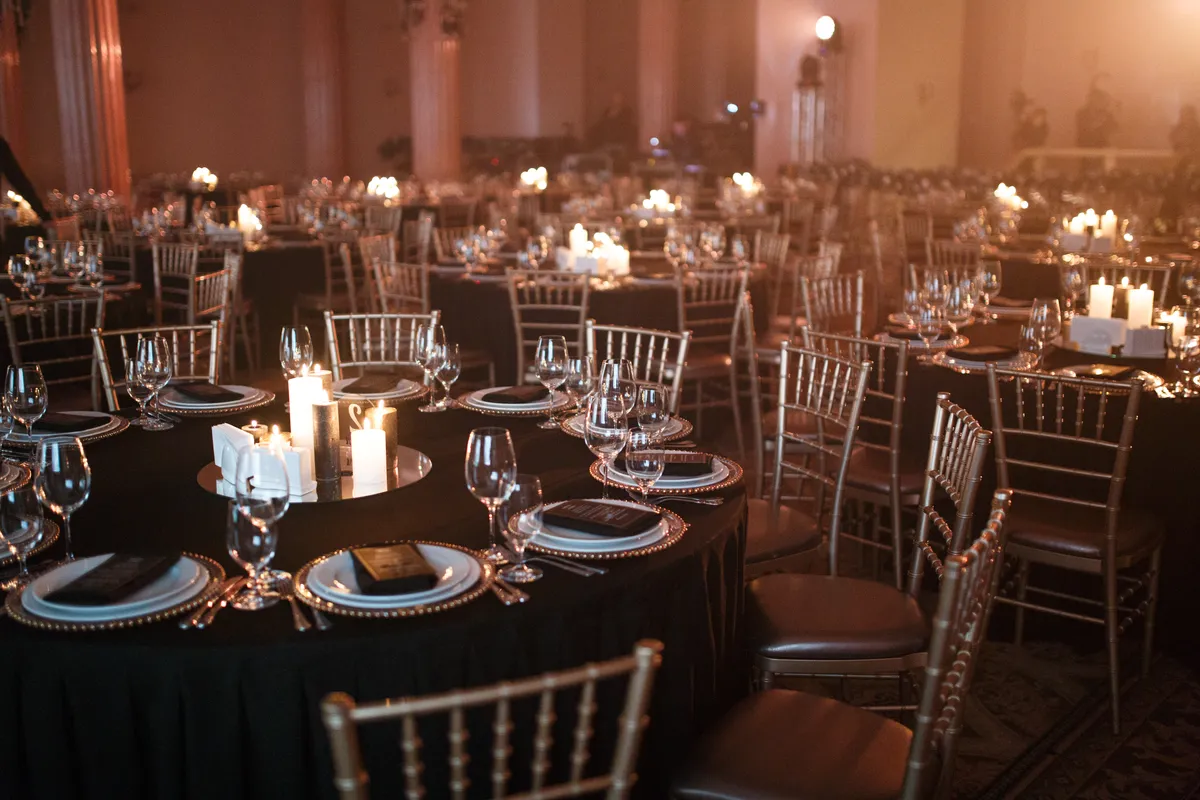 Formal gala dinner setting with long tables in a grand venue and warm moody lighting